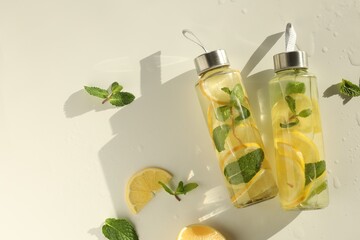 Lemon water with mint in bottles, fresh fruits and leaves on white table, flat lay. Space for text
