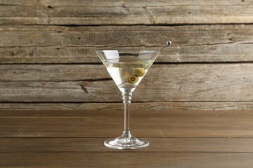 Martini cocktail with olives in glass on wooden table