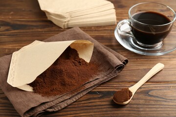 Paper filter, ground coffee and cup of drink on wooden table