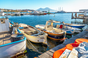 Obraz premium Fishing boats at the pier in the port of Naples on a sunny day with Mount Vesuvei in the background
