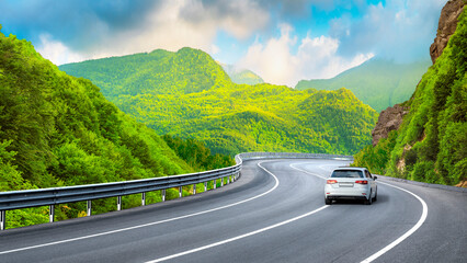 White car driving on nature road between green mountains in summer. Nature landscape on highway for...