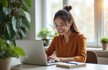 Happy young woman works remotely at home. Sits at bright home office desk. Plants, notebooks around. Using laptop. Work setup organized. Home office filled with greenery. Cozy home atmosphere. Remote