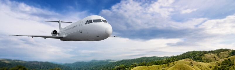Obraz premium Commercial airplane flying in the sky above the mountain range with cloudscapes background
