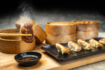 Human hand with chopstick eat fried chinese dim sum dumpling, gyoza, jiaozi or mandu with soy sauce on the table. Food for breakfast, lunch or dinner