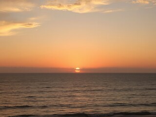 Fototapeta premium Golden hues of the setting sun painting the sky in warm tones over the tranquil Pacific Ocean, water, reflection