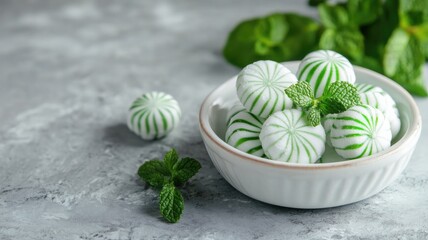 White and green striped peppermint candies in bowl with mint leaves