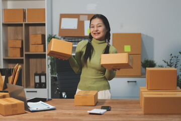 Startup SME small business entrepreneur of freelance Asian woman wearing apron using laptop and box to receive and review orders online to prepare to pack sell to customers, online sme business ideas.