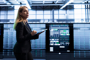 Manager in server room using tablet to implement and maintain security measures, protecting systems...