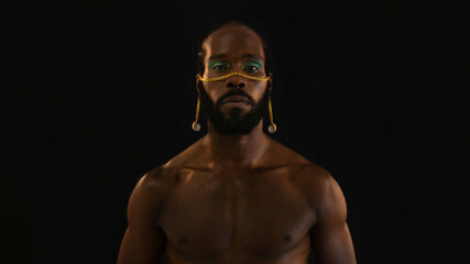 Serious African American shirtless gay model posing over black background. Portrait of arrogant...