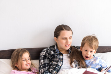 happy family. Close up loving mother lying with daughter son two kids pajamas in bed children reading interesting storybook, preschool smiling kid girl enjoy fairytale before go to sleep good pastime