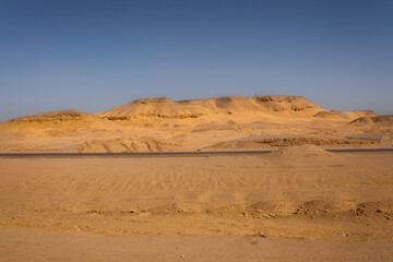 Desert landscape with sand dunes, blue sky and empty road.