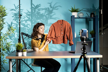 Fashion designer presenting newly created stylish jacket to viewers, showcasing fabric details,...