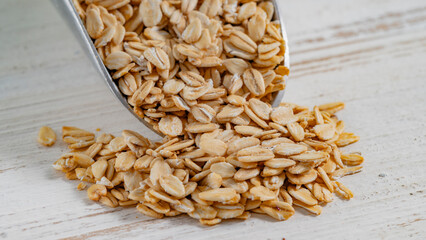 Rolled oats spilling from a metal scoop onto a rustic white wooden surface. Perfect for natural...