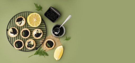 Tasty tartlets with black caviar on green background with space for text
