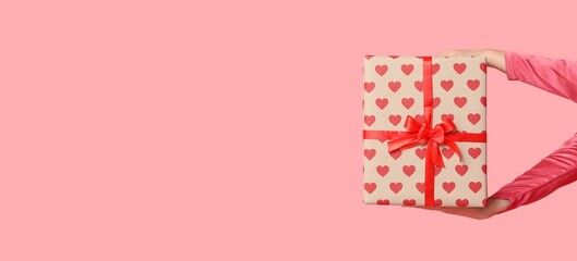 Female hands holding gift box on pink background with space for text. Valentine's Day celebration
