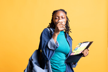 Woman closing eyes and enjoying delicious coffee while examining clipboard with colorful sticky...