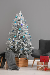 Beautiful Christmas tree with gift boxes and armchair near grey wall