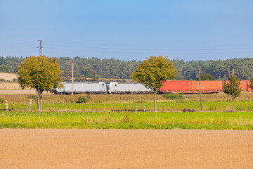 white train with red goods wagons across a field
