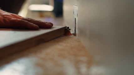 Carpenter in studio puts wood block through spindle moulder, creating smooth edges on wooden pieces. Cabinetmaker in joinery using heavy machinery to craft joints for furniture, camera A close up