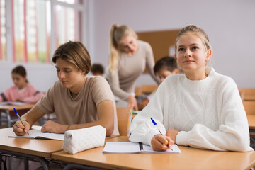 Teenage girl and boy sitting together at desk and doing tasks in classroom.