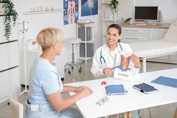 Obraz premium Female endocrinologist showing structure of thyroid gland to mature woman at table in clinic