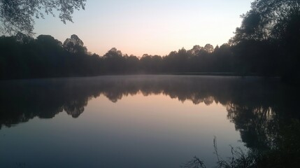 Fototapeta premium A tranquil lake reflecting the soft colors of dawn with mist rising from the water.