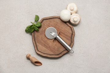 Wooden board with stainless steel pizza cutter and mushrooms on light background