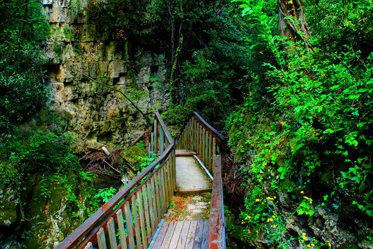 Daring scenery with a bridge from Sentiero Li Vurgacci in Pioraco, the tight wooden structure surrounded by impressive rocks, wild greenery, trees, and the Potenza river's waters flowing under it