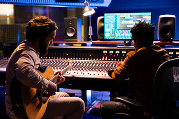 Musician records electro acoustic guitar sounds with technician in studio, doing mix and master...