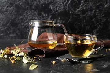 Cup and teapot of tasty linden tea on black background