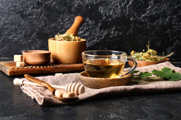 Cup of tasty linden tea with wooden dipper, spoon and sugar cubes on black background