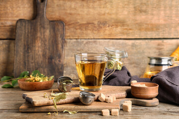 Boards with cup of tasty linden tea, sugar cubes and metal infuser on wooden background
