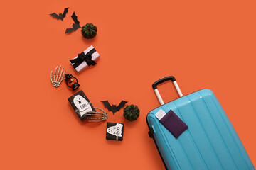 Suitcase with different Halloween decorations, passport and gift boxes on orange background