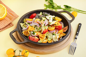 Frying pan with delicious Italian pasta salad on light yellow background