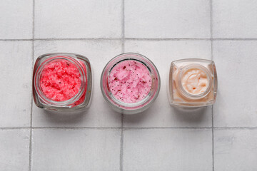 Jars with scrubs and cosmetic cream on light tile background