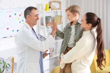 Fototapeta premium Male speech therapist giving high-five to little boy and mother in office
