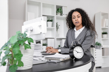 Alarm clock on table against businesswoman trying to meet deadline in office, closeup