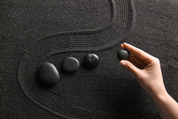 Female hand and stones on black sand with lines. Zen concept
