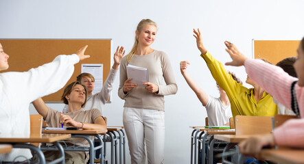 Group of positive children raising hands to answer during lesson at classroom in secondary school