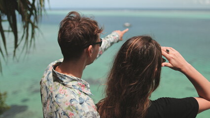 A man and a woman standing side by side, looking out at the vast expanse of the ocean, waves crashing against the shore.