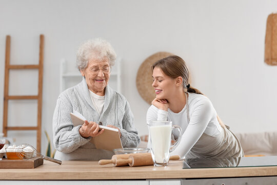 Young woman and her grandmother with recipe book baking in kitchen
