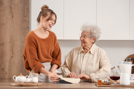 Young woman and her grandmother cooking pie with baking dish at table in kitchen