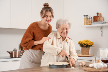 Young woman and her grandmother cooking pie with baking dish at table in kitchen