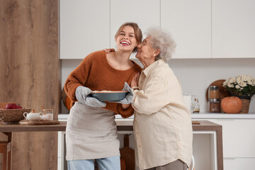 Senior woman kissing her granddaughter with tasty pie in kitchen