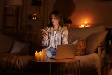 Young woman with laptop using mobile phone at home during blackout