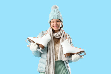 Young woman in winter clothes with ice skates on blue background