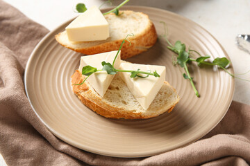 Plate with bread, triangles of tasty processed cheese, micro green and napkin on light table, closeup