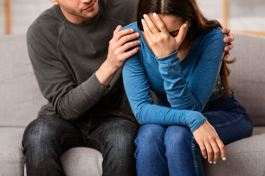 Compassion Concept. Man comforting and consoling his sad mourning friend embracing her sitting on couch