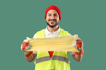 Male scavenger with roll of garbage bags on green background