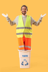Male scavenger in recycle trash bin for plastic on yellow background